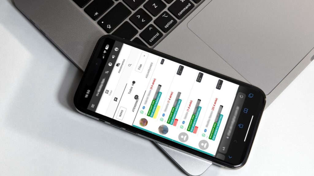 Um iphone sobre um macbook em uma mesa, mostrando a tela do EkmChat com todos os canais de atendimento centralizados.